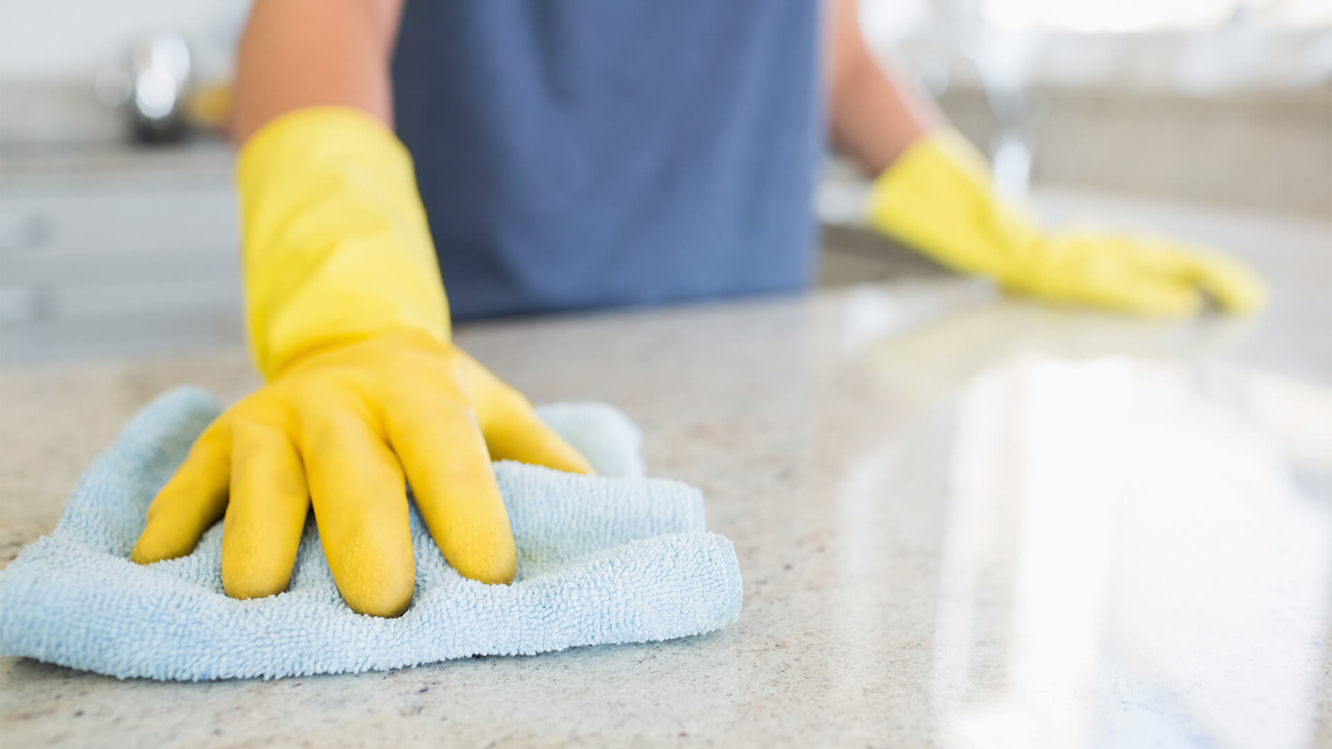 Closeup of person wearing rubber gloves cleaning a kitchen surface