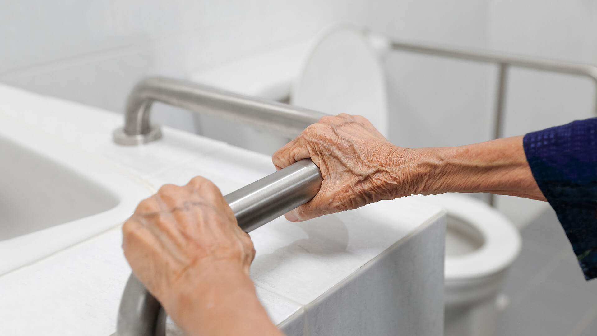 Closeup of an older person using a grab bar in a bathroom