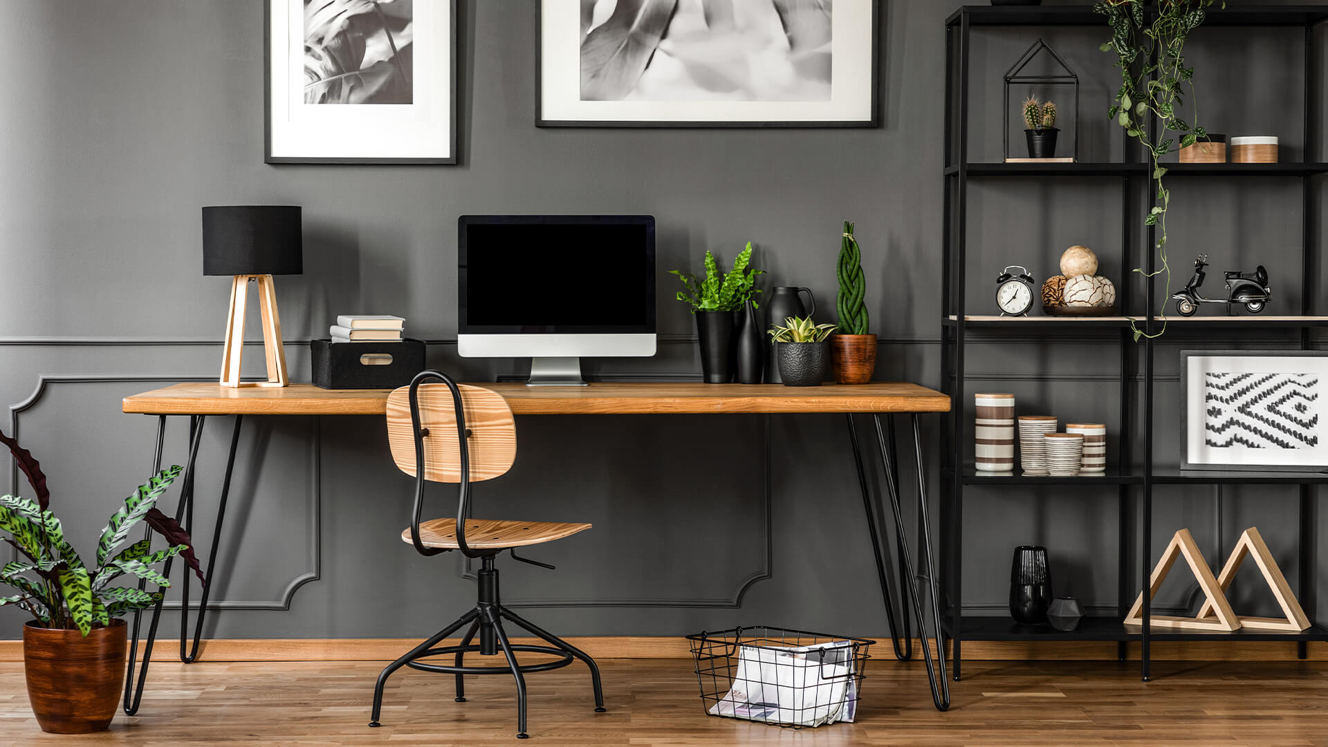 Home office interior. The space is modern with charcoal grey walls, and open iron shelving, and many plants