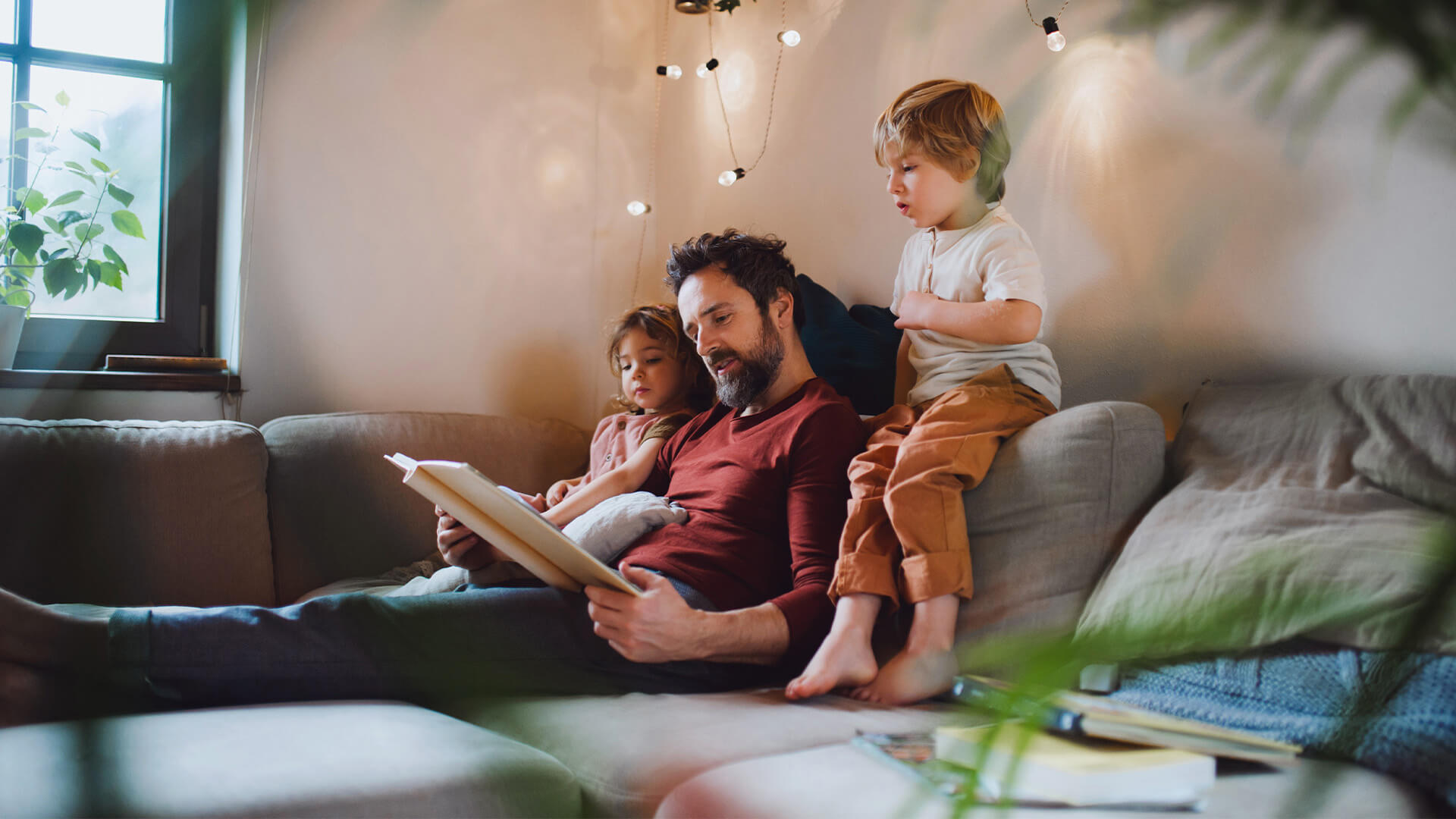 Dad and 2 kids sat on a sofa reading together