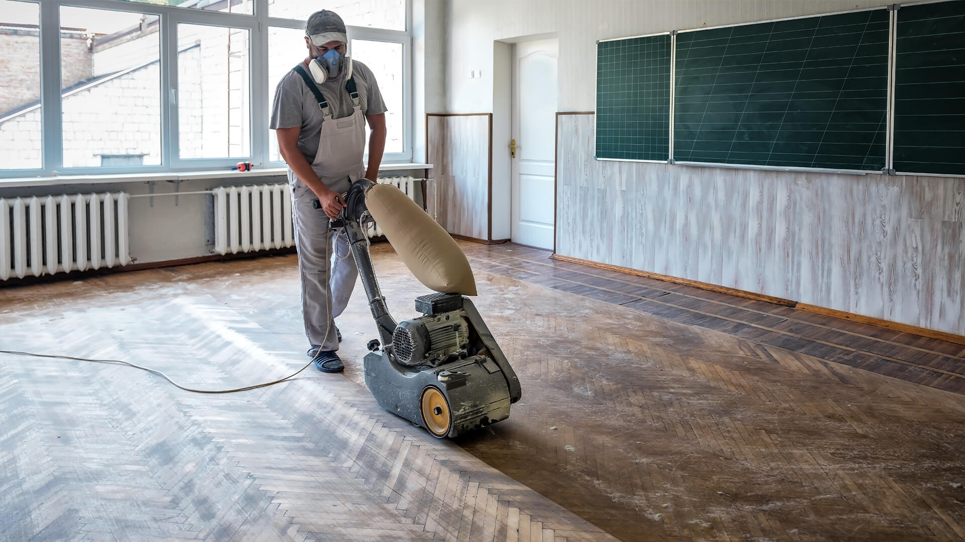 Worker polishing hardwood parquet floor with grinding machine